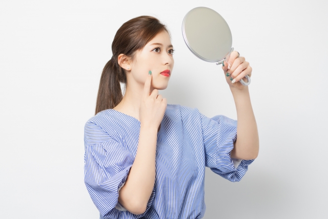 切らない小顔整形のデメリットを説明する人差し指を頬に当てて鏡を見る女性のイメージ図