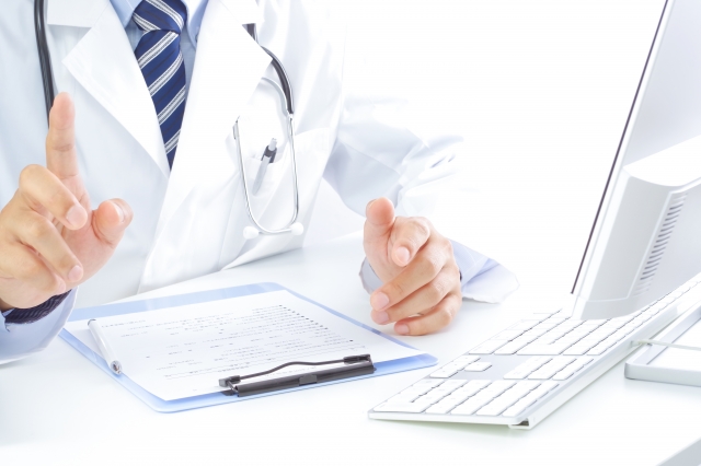 医師が机に座りPCと書類を前に話している様子
