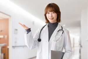 白衣の女性医師が手のひらを上に向けて案内する