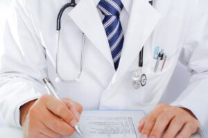 聴診器を首にかけペンで書類に記入する医師