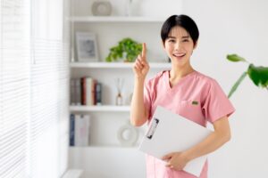医療従事者の女性が指をさしながら笑顔で立つ