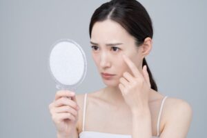 鏡を見ながら目元のたるみをチェックする女性