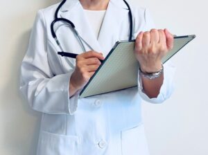 白衣を着てバインダーにメモする医療従事者