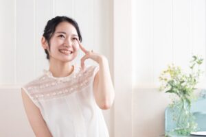白い服を着た女性が笑顔で顔に手を添える