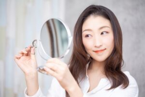 鏡で自身の顔を見る女性とビューラー
